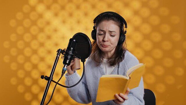 Voice actor reads book while enjoying coffee, recording audiobook using microphone, studio background. Woman using mic and headphones to produce digital recording of novel, drinking beverage, camera B
