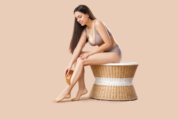 Young woman in underwear massaging her leg with wooden scraper on beige background - obrazy, fototapety, plakaty