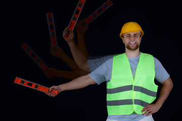 Stroboscopic photo of male builder in reflective vest with level on dark background