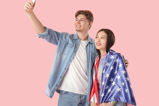 Young couple with flag of USA taking selfie on pink background