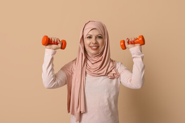 Muslim female fitness trainer exercising with dumbbells on beige background