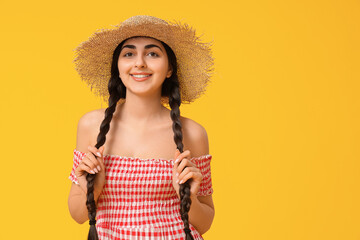 Beautiful young happy woman in straw hat on yellow background. Festa Junina (June Festival) celebration