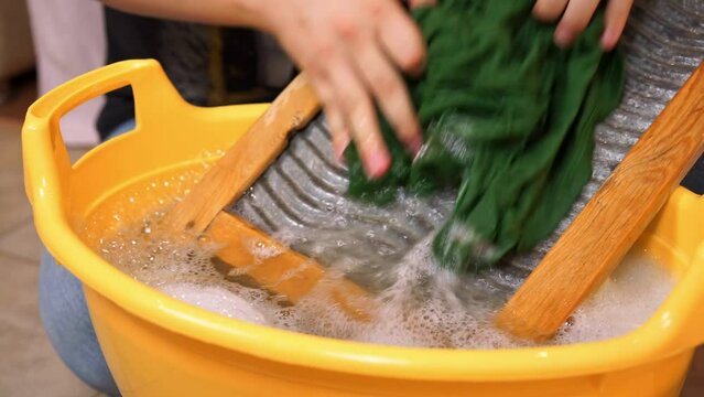 Woman diligently washes clothes by hand using washboard. Laundress skillfully uses old washboard and basin for washing dirty clothes
