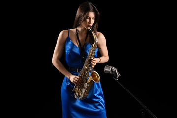 Beautiful woman with microphone playing saxophone on dark background