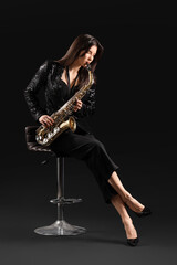 Obraz na płótnie Canvas Beautiful young woman playing saxophone on dark background