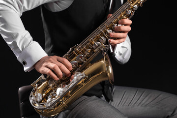 Male artist playing saxophone on black background, closeup
