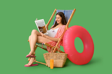 Beautiful young pregnant woman with magazine and bottle of sunscreen cream sitting on deck chair...