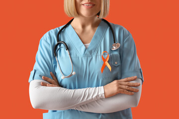 Beautiful mature happy female doctor pointing at ribbon on orange background, closeup. Multiple...