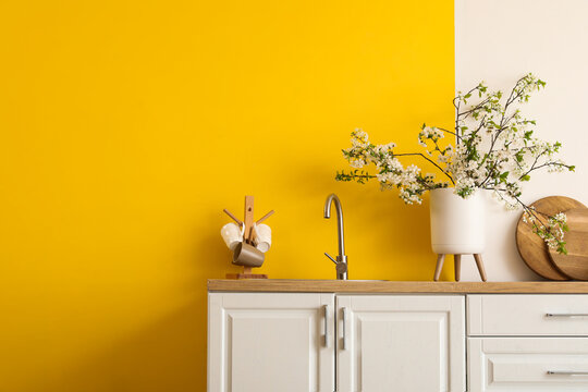 Vase with blooming branches on white counter in yellow kitchen