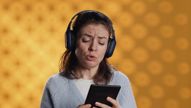 Voice actor frowns while reading ebook, portraying character, studio background. Woman reenacting digital recording of novel, interpreting furious antagonist, reading text from tablet, camera A