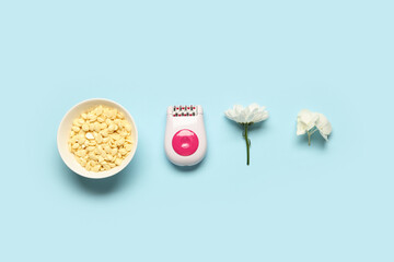 Modern epilator with wax and flowers on blue background