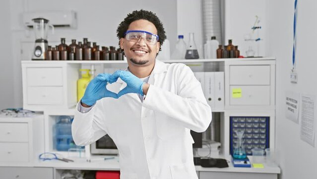 A smiling, young african-american male scientist, cheerfully making a heart symbol with his hands in a lab, radiating love.
