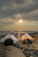 Couple on a picnic lying holding hands looking at the sky on the beach
