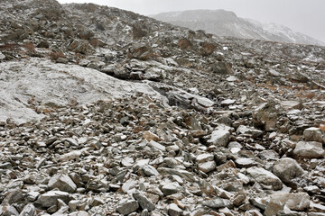 View from below on the steep slope of the mountain range with a scattering of large stones powdered with the first snow.