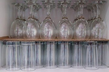 A row of clear glasses are lined up on a shelf