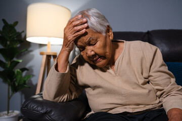 senior woman suffering from stress or a headache while sitting on sofa in living room at night