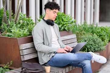 Young man freelancer sitting outdoors and working on laptop