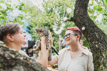 Two cheerful women playing with a kitten during a friends summer party in a country house