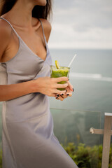 Close up photo of fresh green detox cocktail and a smiling girl holding it , sea view on background