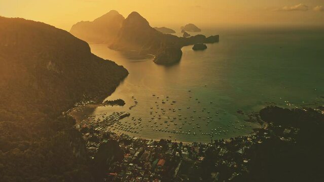 Aerial view sunset at island mountain harbor bay. Oceane town lagoon in cinematic sun light. Philippines, El Nido Islands, Palawan. Sea ships, vessels, boats, yachts at sand coast. Buildings at shore