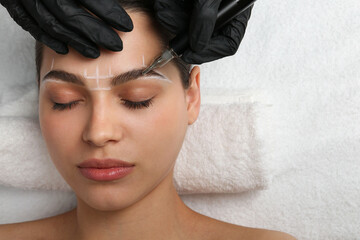 Beautician making permanent eyebrow makeup to young woman, top view. Space for text