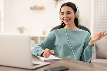 Young woman in headphones using video chat during webinar at table in room