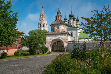 View of the Holy Gates of the Alexander Monastery, the Church of the Ascension and the bell tower on a sunny summer day, Suzdal, Vladimir region, Russia - obrazy, fototapety, plakaty