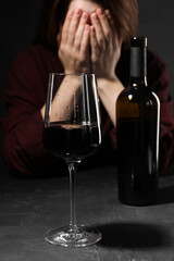 Alcohol addiction. Woman covering her face at dark textured table, focus on glass of red wine