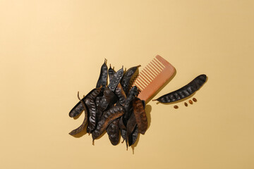 A wooden comb placed on light brown table surrounded by some black locust fruits with blank space...
