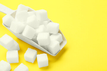 White sugar cubes and scoop on yellow background