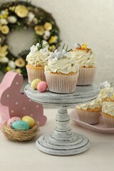 Tasty Easter cupcakes with vanilla cream and festive decor on light wooden table