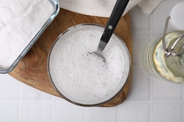 Chemical reaction of vinegar and baking soda in glass bowl on white tiled table, top view