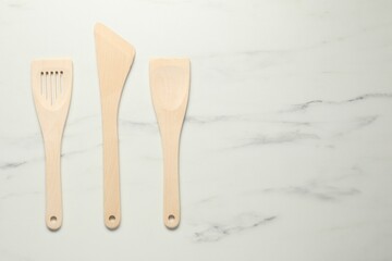 Different wooden spatulas on white marble table, flat lay. Space for text - obrazy, fototapety, plakaty
