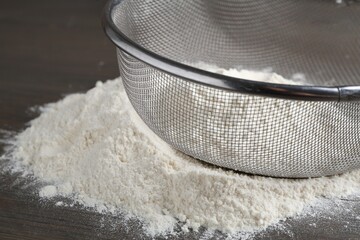 Metal sieve with flour on wooden table, closeup