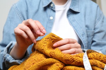 Woman sewing sweater with needle, closeup view