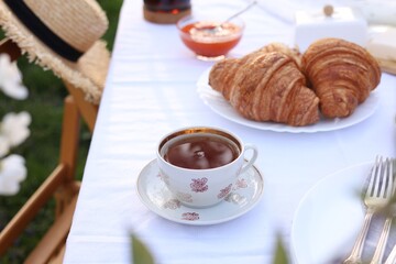 Stylish table setting with tea and croissants in spring garden