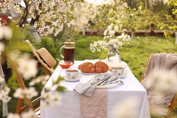Stylish table setting with beautiful spring flowers, tea and croissants in garden
