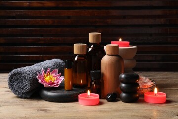 Different aromatherapy products, spa stones, towel and flower on wooden table