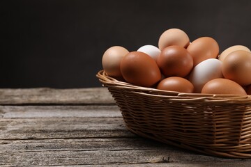Fresh chicken eggs in wicker basket on wooden table. Space for text
