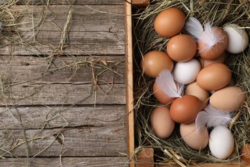 Fresh chicken eggs and dried hay in crate on wooden table, top view. Space for text