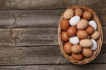 Fresh chicken eggs in wicker basket on wooden table, top view. Space for text