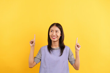 Young women pointing finger up with both hands to present something isolated on yellow background