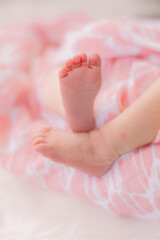 A pair of newborn feet and legs. The baby girl is wrapped up in a pink blanket.