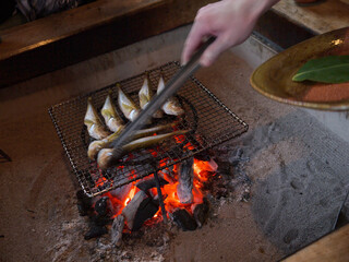 Grilling Japanese ayu sweetfish for dinner on glowing coals in traditional irori hearth
