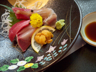 Luxury Japanese sashimi with tuna, ebi shrimp, hamachi amberjack fish and Aka Uni sea urchin roe on ceramic plate decorated with yellow Chrysanthemum flower 