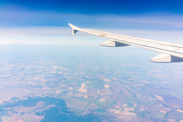 Fototapeta premium Aerial view from airplane window above green ground. View from the airplane window with beautiful clouds at sunrise