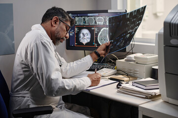 Professional radiographer working with brain X-ray image making notes in medical record, medium shot