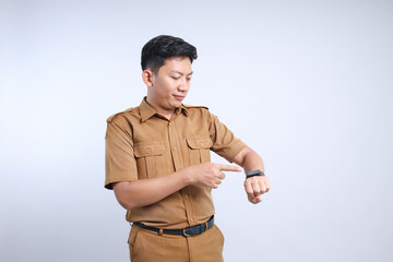 Male Asian civil servant in brown uniform pointing at wrist watch and smiling, showing smartwatch...