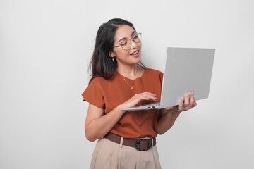 Smiling young woman wearing brown shirt and eyeglasses while holding laptop to work or browsing isolated over white background.