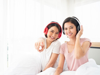 Joyful young Asian women wearing headphones in a bright room, one pointing at the camera sharing a...